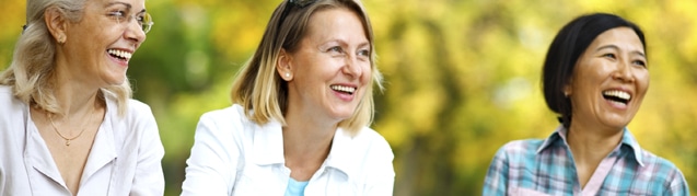 an image of 3 happy mature woman who are outdoors. @ of them are blonde caucasians and one of them is an asian woman