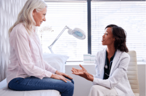 Mature Woman In Consultation With Female Doctor Sitting On Examination Couch In Office