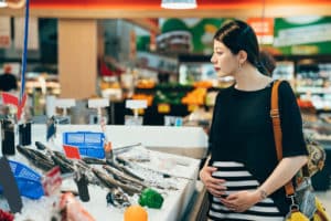 Happy pregnant female customer choosing and buying fish in shop.