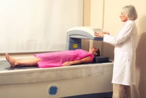 Female doctor examining woman in 40s at Bone Densitometer Machine.