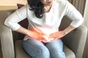 A cropped shot of a woman with pelvic pain bent over in a chair